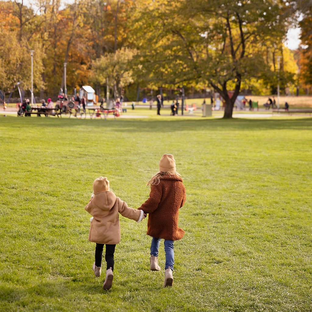 Två barn springer på en gräsmatta mot en lekpark.