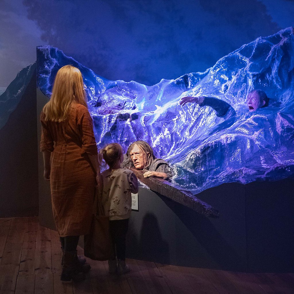 Helena Elm och ett barn står framför en vaxdocka i ett konstgjort hav.