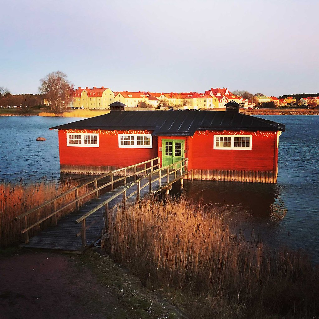 A red wooden house with a black roof built directly on the water.