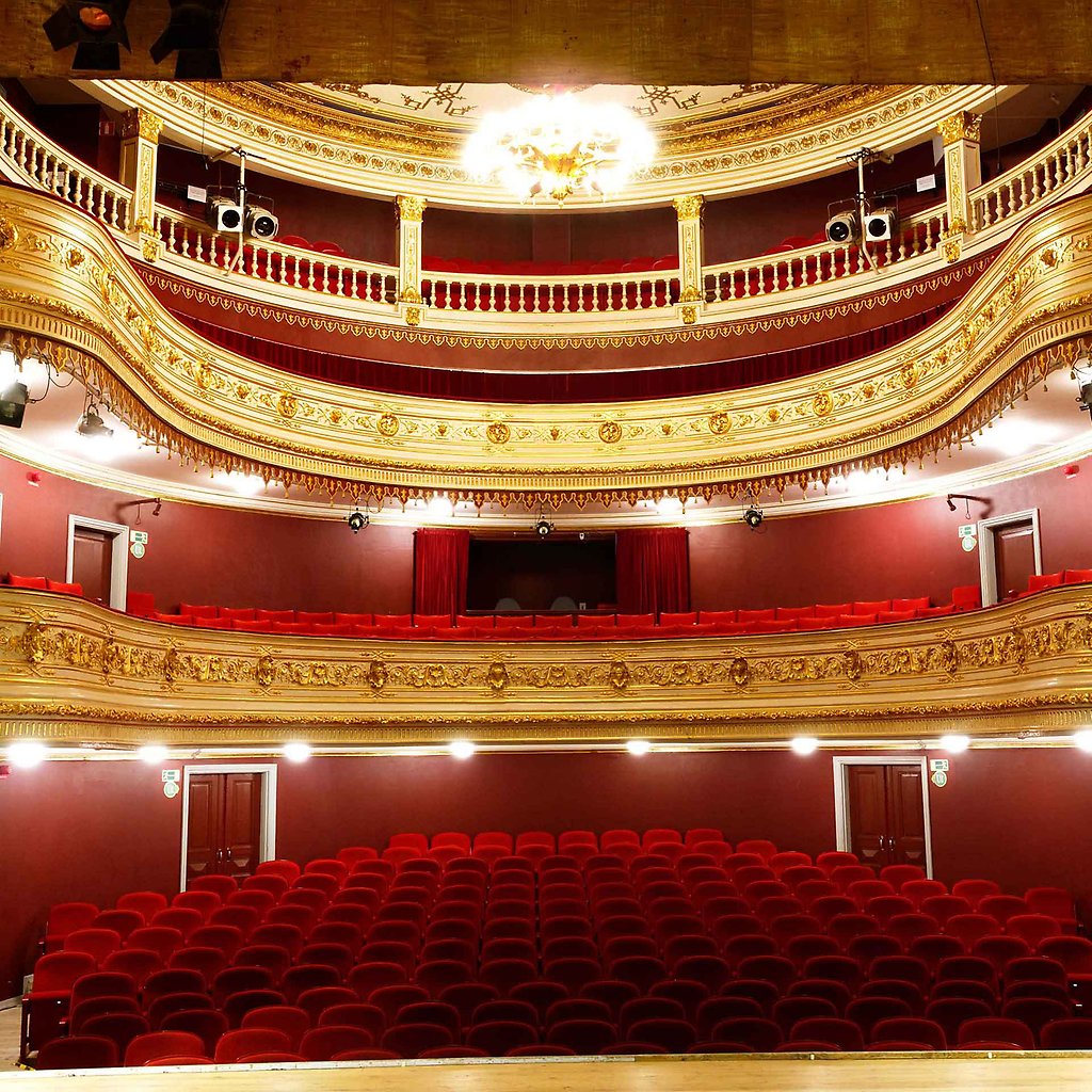 The interior of Kalmar Theatre with red chairs, golden ornaments on the balconies and a chrystal chandelier. 