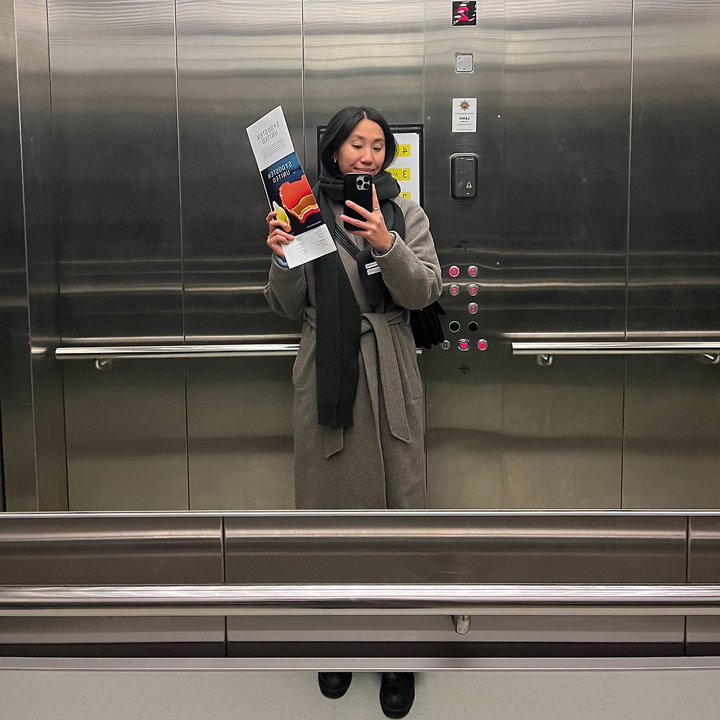 Thuha Nguyen står i en hiss och håller upp en broschyr.
