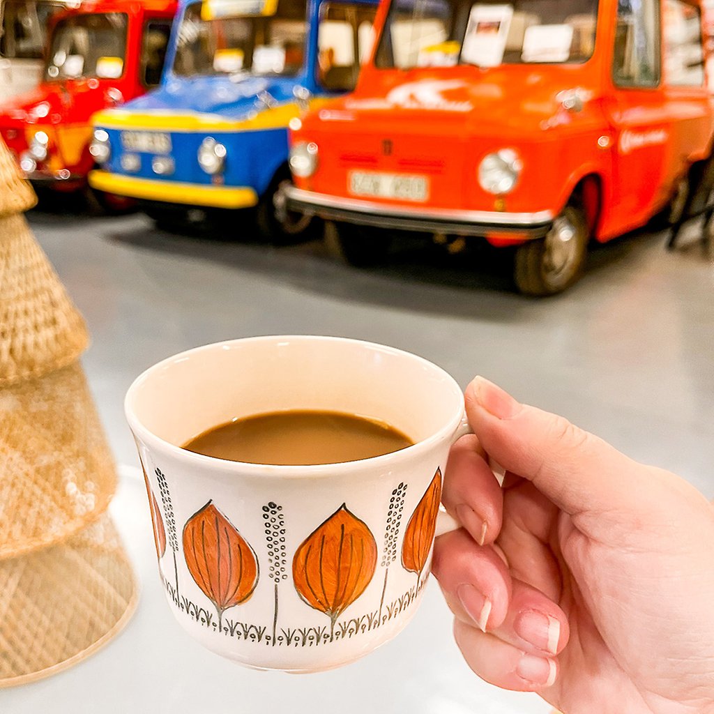 I förgrunden håller en hand en fylld kaffekopp och i bakgrunden syns tre Tjorvenbilar.