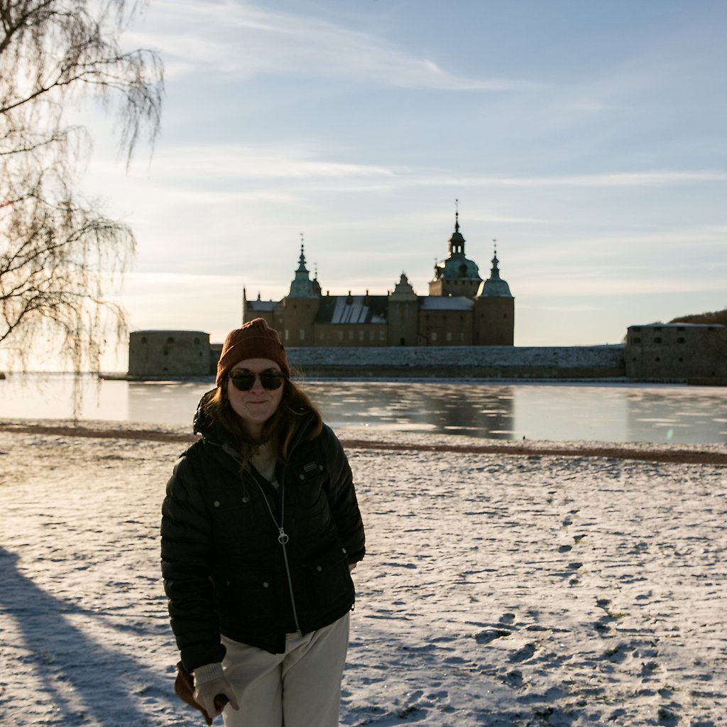 Sara Zetterström, iklädd mössa och solglasögon, står framför Kalmar Slott i ett vinterlandskap