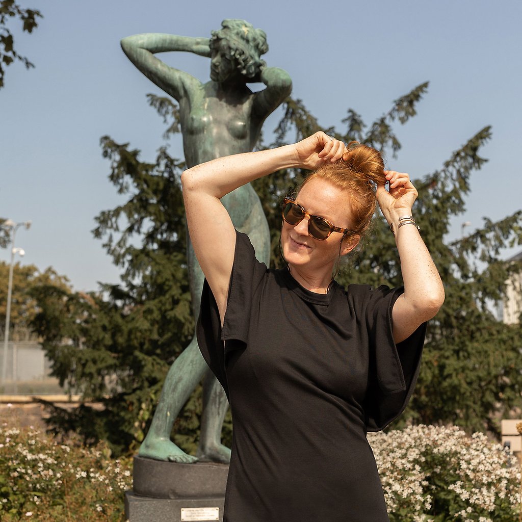 Sara står framför en skulptur och poserar likadant som skulpturen. Den föreställer en kvinna som sätter upp sitt hår.