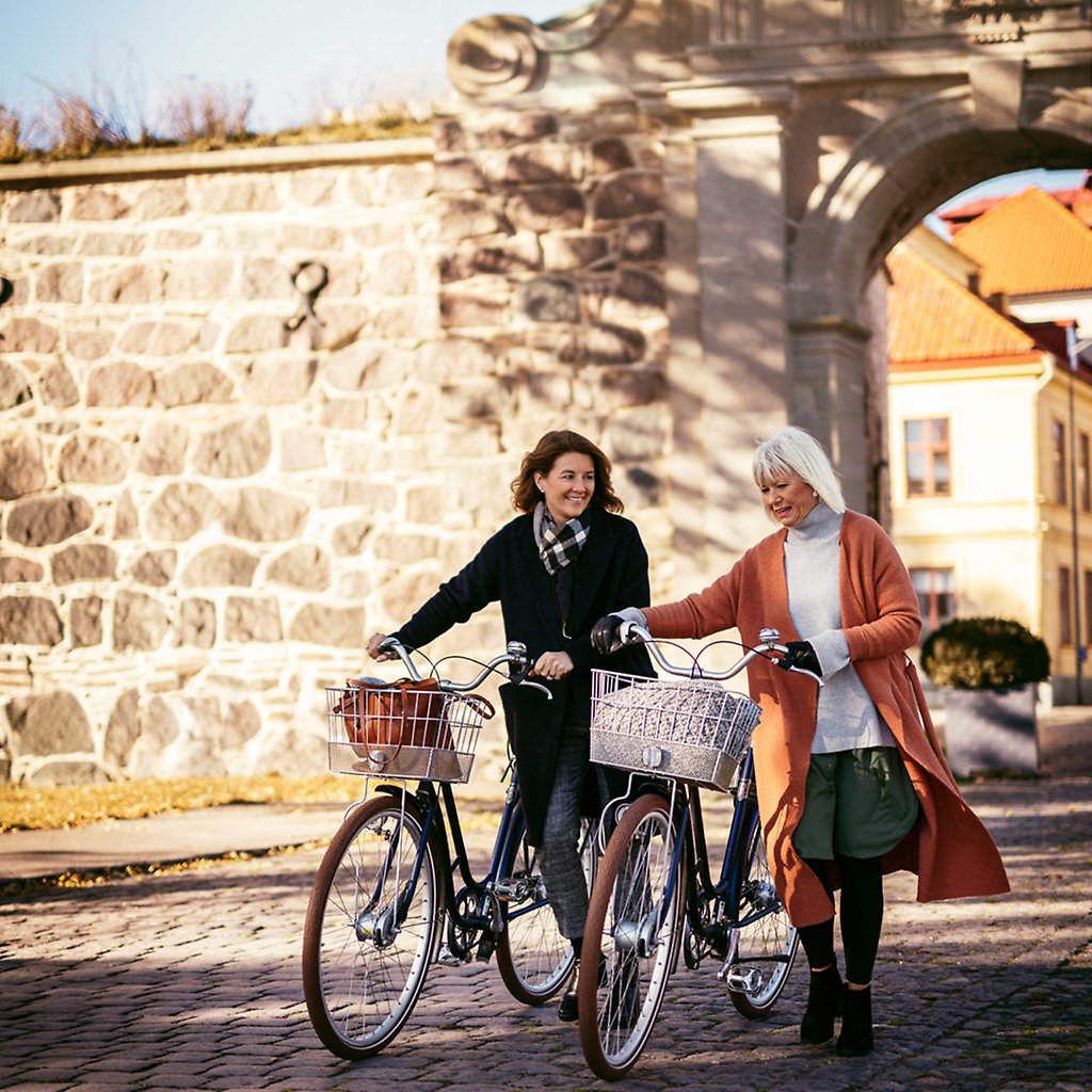 Two women with bikes in front of the city wall. 