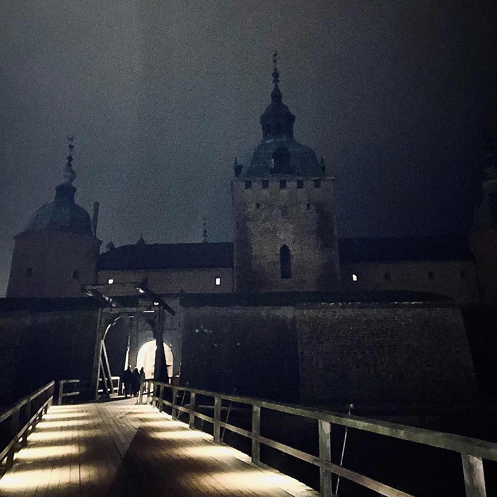 Vägen upp till Kalmar Slott i mörker. På håll syns några personer som går genom porten.