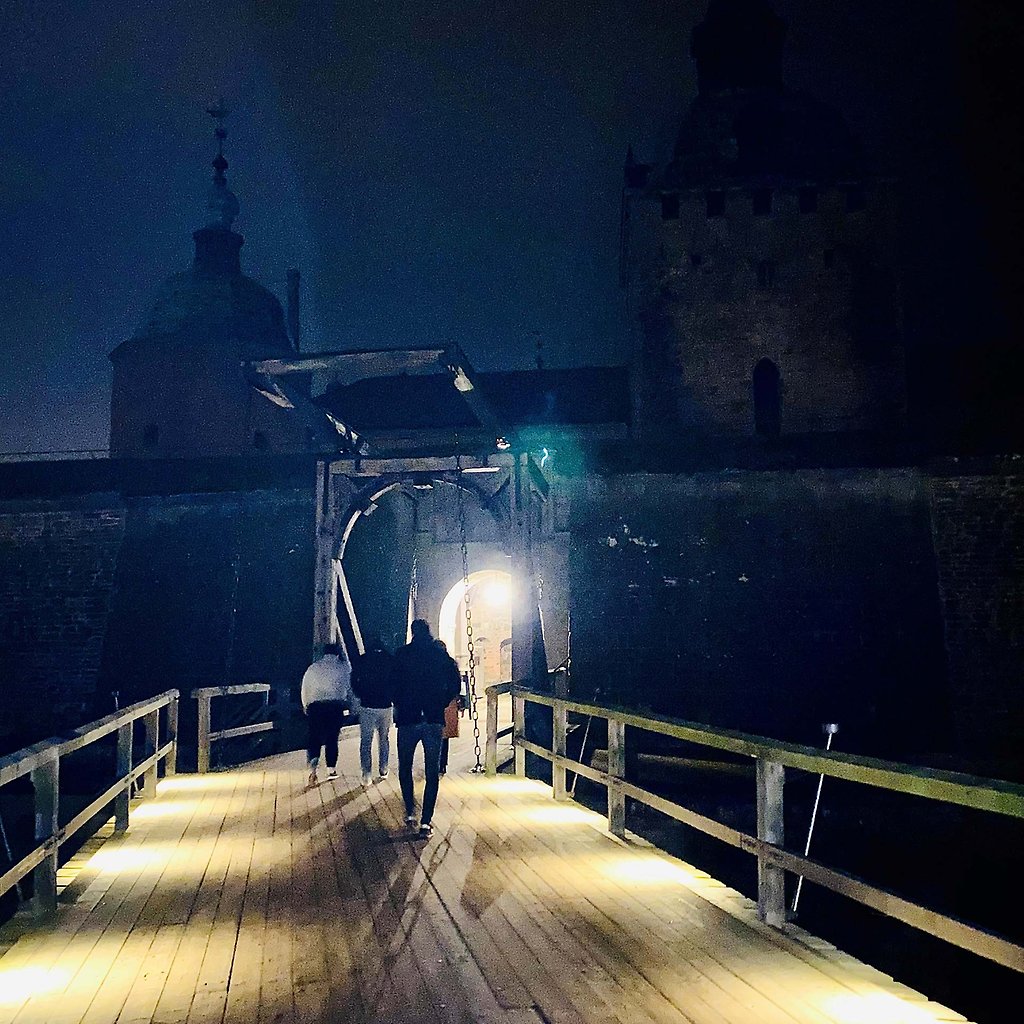 Tre personer går i mörkret genom valvet vid ingången till Kalmar Slott.