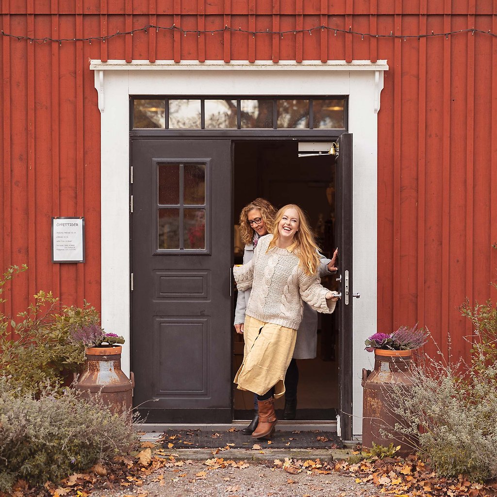 Marija och Helena står i dörröppningen till ett rött trähus.