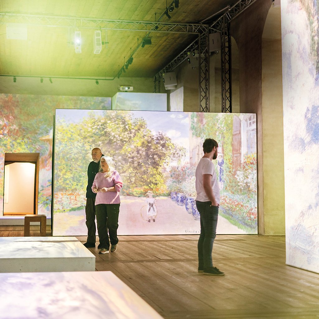 Monets målningar projiceras på stora skärmar. I lokalen syns också siluetter av personer som tittar på bilderna.