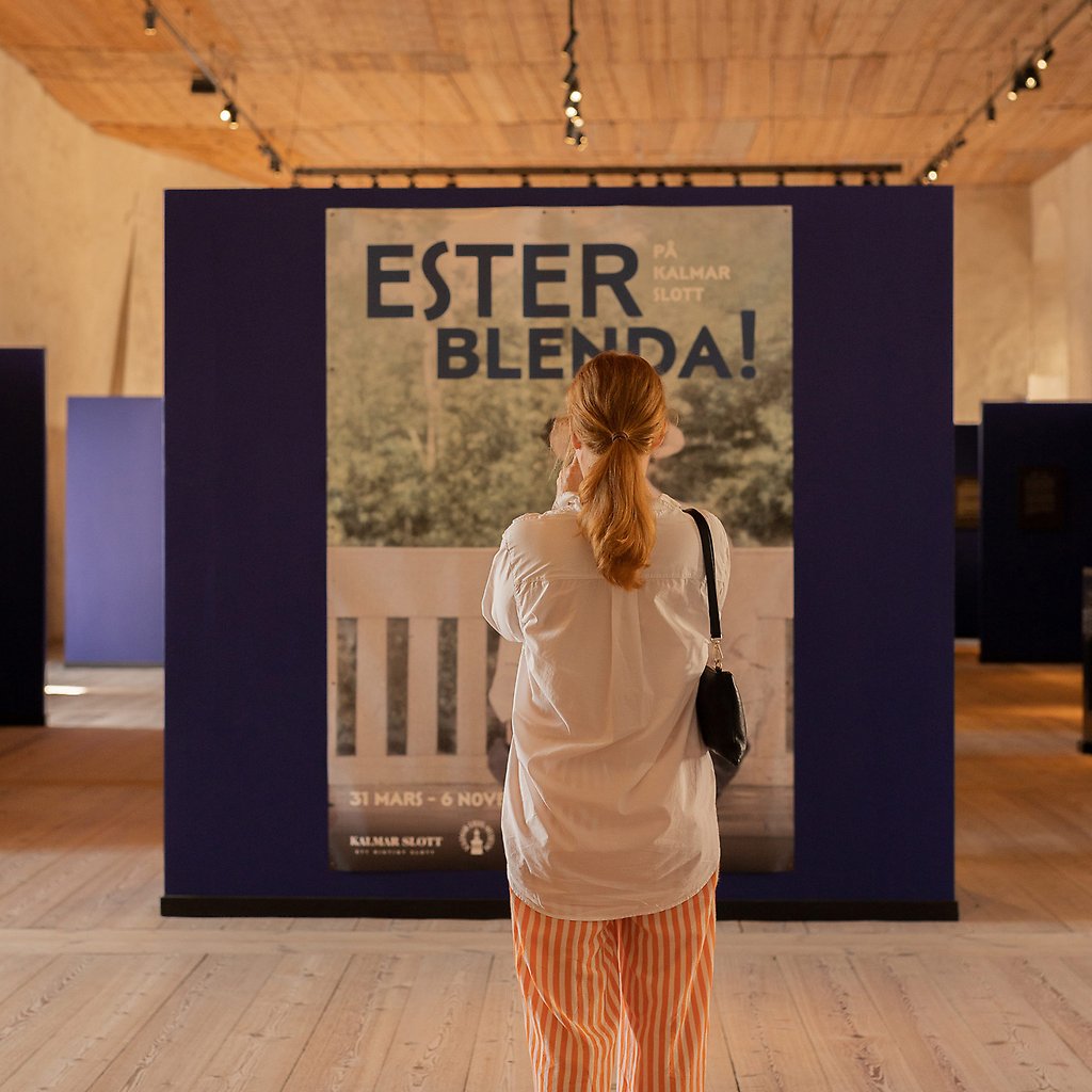 Sara Zetterström står och tittar på en bild i utställningen Ester Blenda.