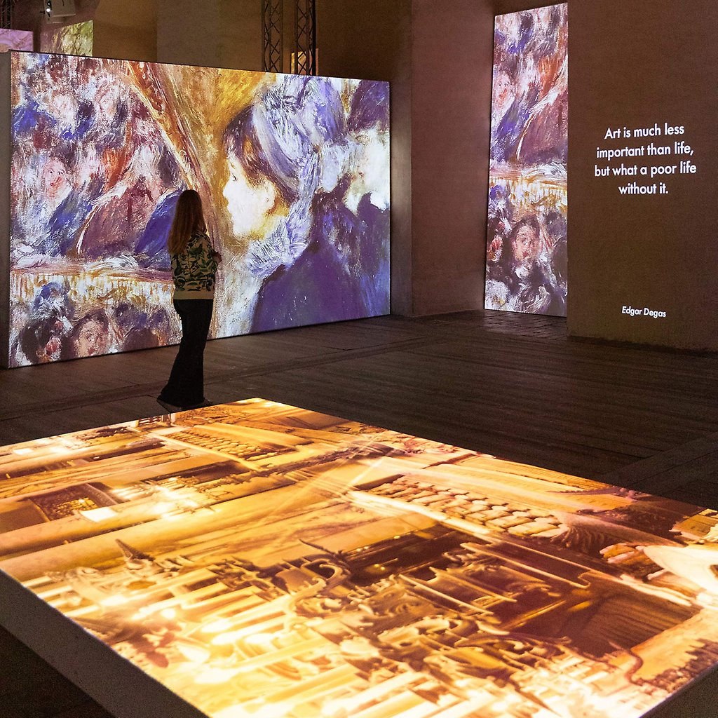 Helena står i utställningen omgiven av stora skärmar, på vilka färgstarka konstverk projiceras.