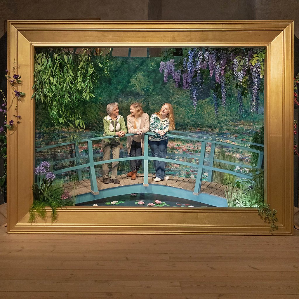 Helena står tillsammans med sin mamma och syster på en Monetbro som är inramad med en stor guldram. 