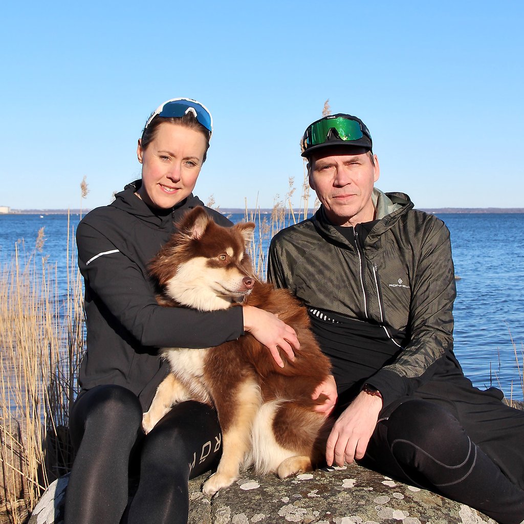 Ulrika och Robban sitter på en sten med havet som bakgrund. Mellan dem sitter en hund.