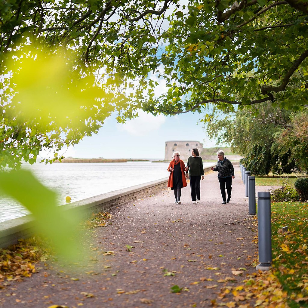 Anneli, Birgitta och Inger strosar på en grusväg som är omgiven av lummiga träd. I bakgrunden syns en del av Kalmar Slott.