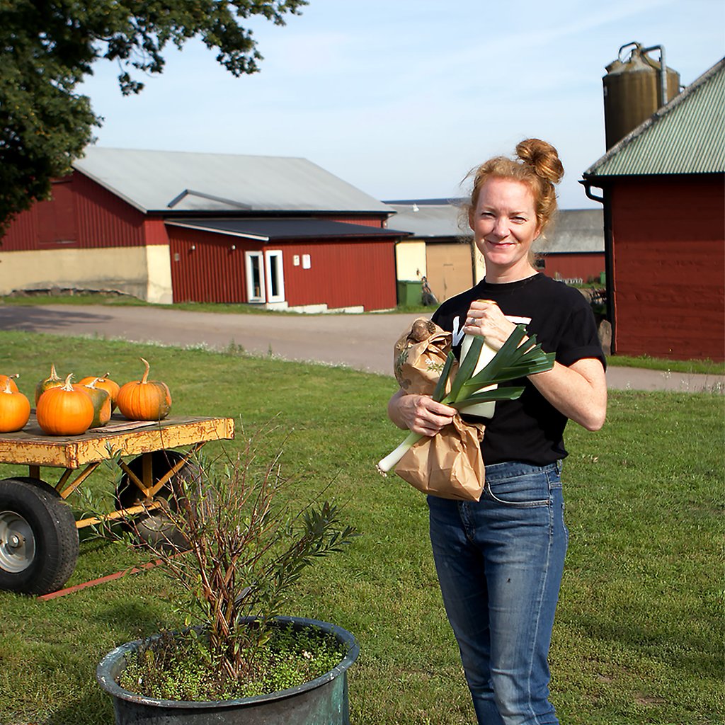 Sara Zetterström står framför en rödmålad lada och håller i grönsaker