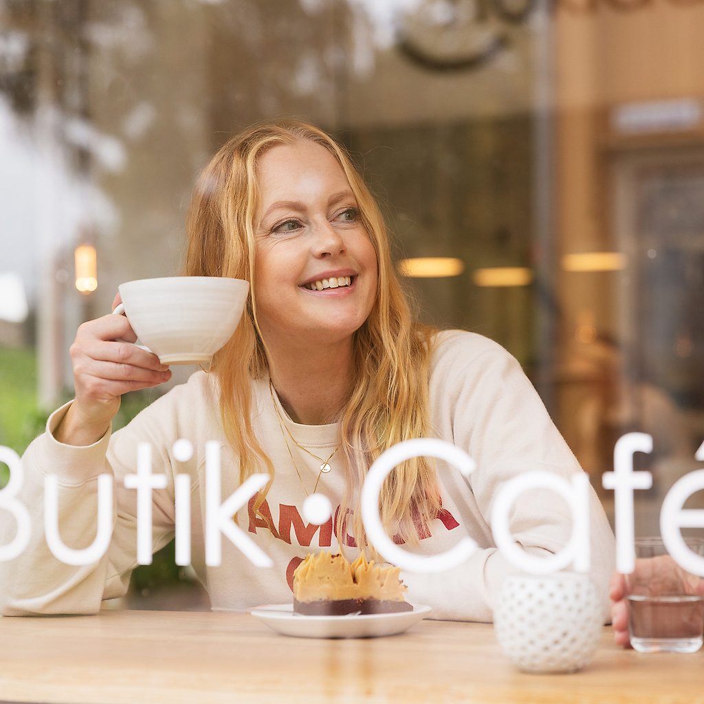 Helena syns genom ett fönster när hon sitter på ett kafé med en kopp kaffe i handen